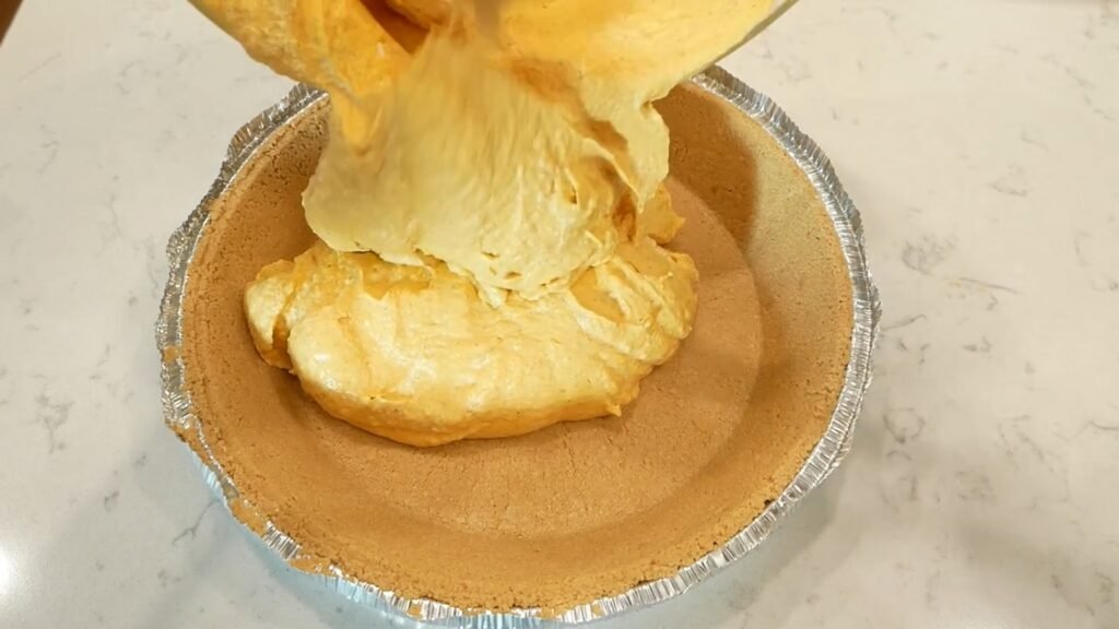 Easy No-Bake Pumpkin Pecan Cheesecake Pouring pumpkin batter into the pie crust