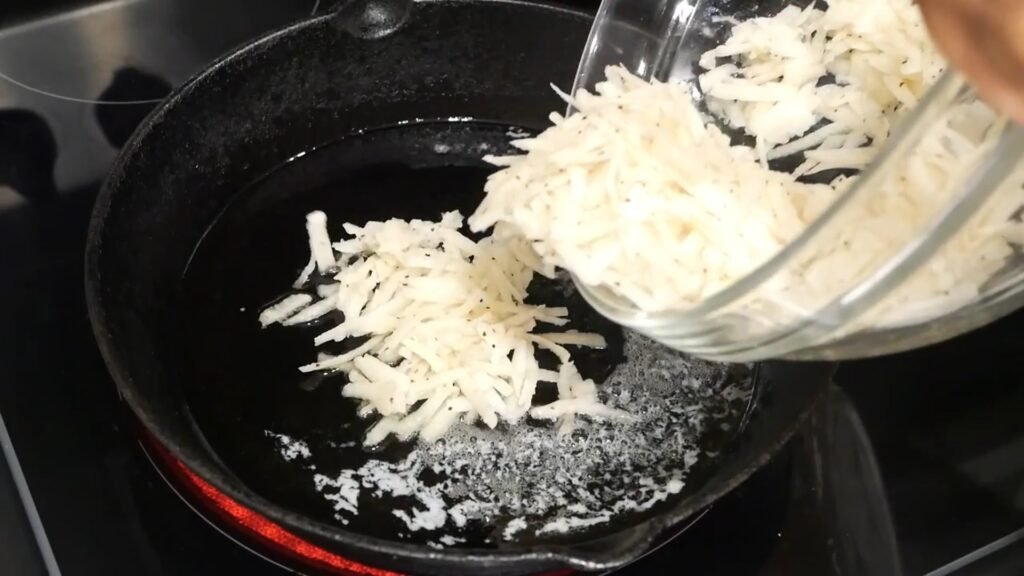 Adding shredded potatoes to skillet